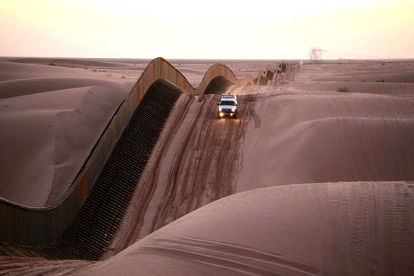 Een grenswacht rijdt langs het hek tussen Mexico en de VS in de woestijn